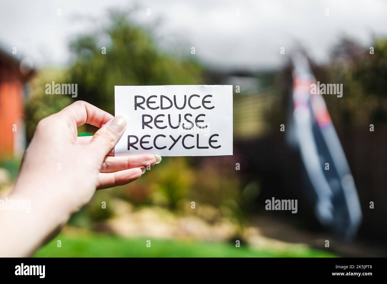 Riduci il segnale di riciclo di fronte al bokeh del cortile con la bandiera australiana sullo sfondo, il concetto di sostenibilità e l'economia circolare Foto Stock