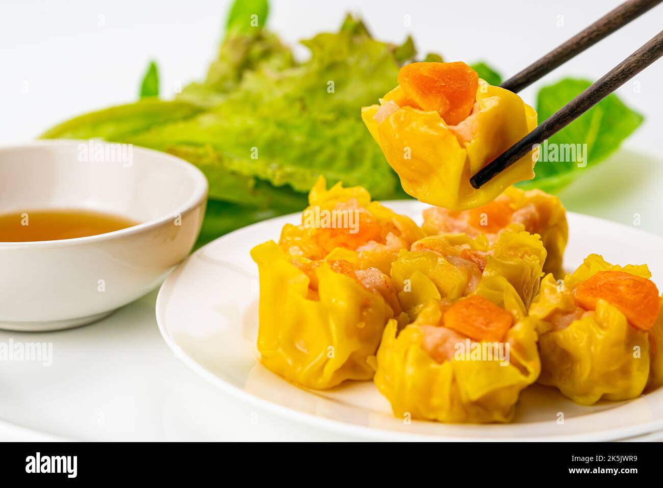 Utilizzando i bastoncini raccogliendo un fresco delizioso gamberetto fatto in casa, maiale tritato e tuorlo d'uovo salato gnocchi al vapore in un piatto di ceramica bianca con salsa in w Foto Stock