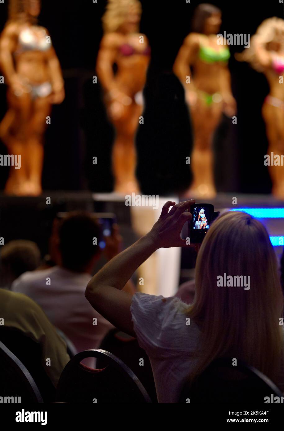 Ha i suoi soldi su uno dei concorrenti. Un membro del pubblico che fotografa le concorrenti femminili con il suo cellulare in un concorso di bodybuilding. Foto Stock