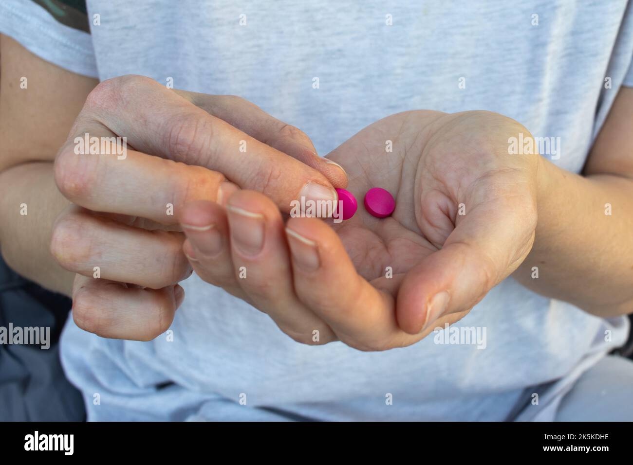 Mano della persona con le pillole. Donna che tiene in mano due pillole rosa. Sanità, concetto di medicina. Il paziente prende il medicamento, i supplementi, gli antibiotici Foto Stock