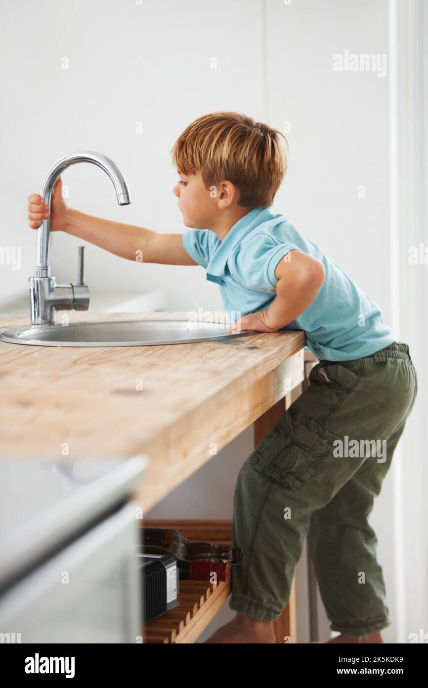Voglio avere un po' d'acqua... Un ragazzo carino che sale sul bancone della cucina per arrivare al rubinetto. Foto Stock