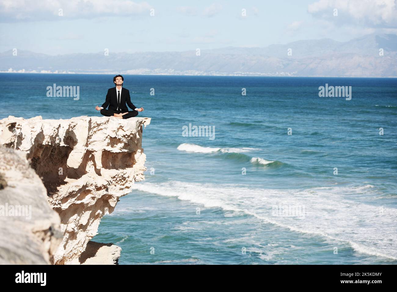 Trovare l'illuminazione in natura. Uomo d'affari seduto e meditato sulla cima di una scogliera sopra l'oceano. Foto Stock