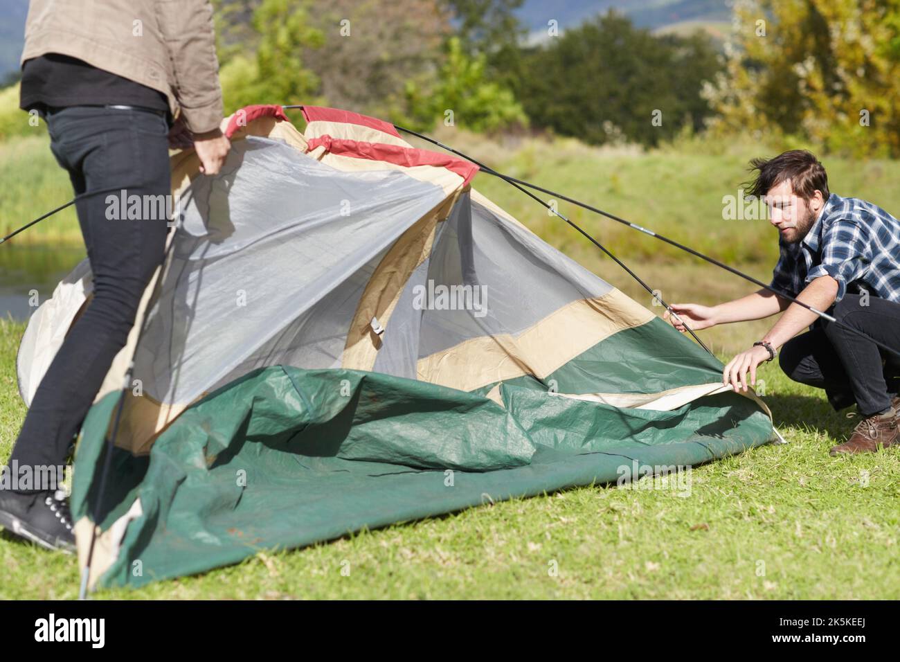 Il lavoro di squadra porta a termine il lavoro. Due giovani uomini che mettono una tenda all'aperto. Foto Stock