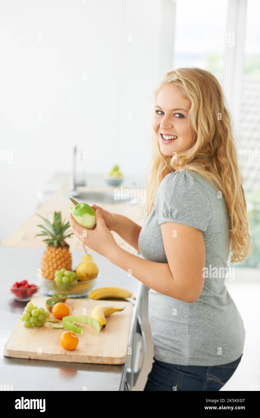 Scegliere cibi sani. Giovane donna curvy e bella che taglia una mela mentre al suo bancone della cucina. Foto Stock Scegliere cibi sani. Giovane donna curvy e bella che taglia una mela mentre al suo bancone della cucina. Foto Stock