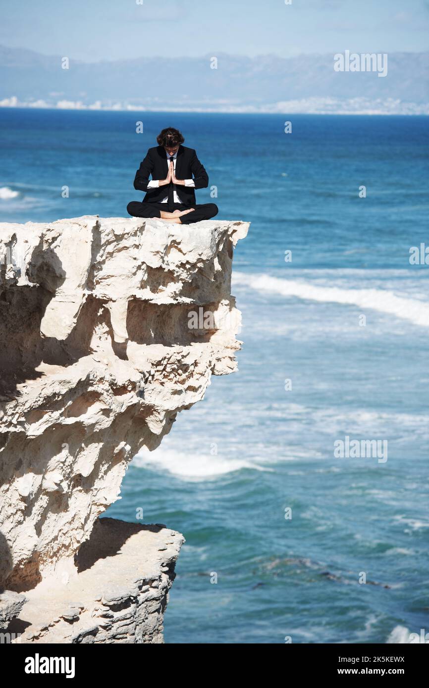Trovare la mia pace interiore. Uomo d'affari meditando sulla cima di una scogliera sopra l'oceano. Foto Stock