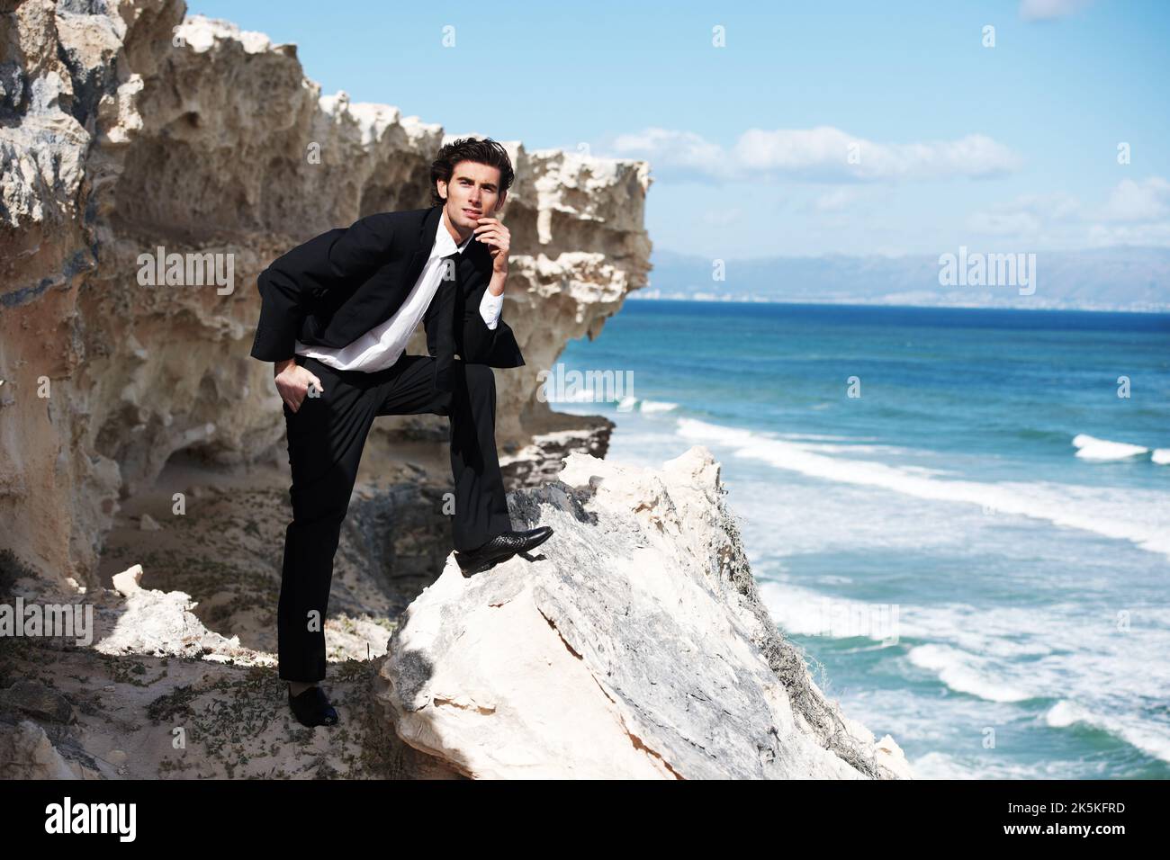 Che bella vista...un bel uomo d'affari che si posa per la macchina fotografica su una roccia che si affaccia sull'oceano. Foto Stock