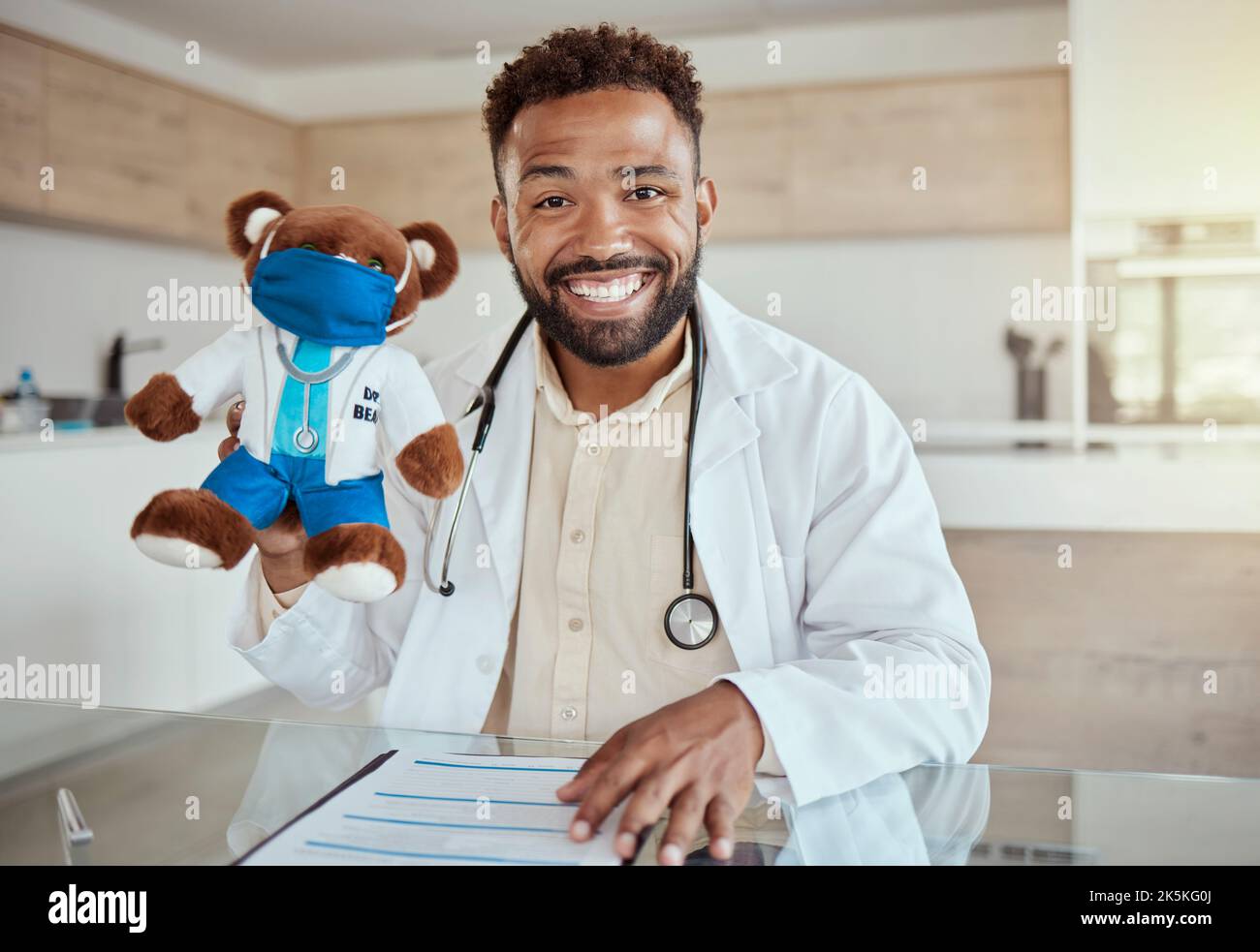 Medico infantile, pediatra e assistenza sanitaria lavorano tenendo un giocattolo orsacchiotto e guardando felice e amichevole mentre si siede nel suo ufficio in un ospedale Foto Stock