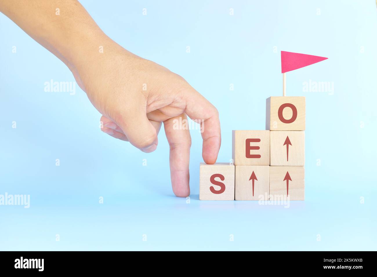 Business SEO o scala di ottimizzazione dei motori di ricerca per il concetto di successo. Uomo scalata a mano blocchi di legno con bandiera rossa. Foto Stock