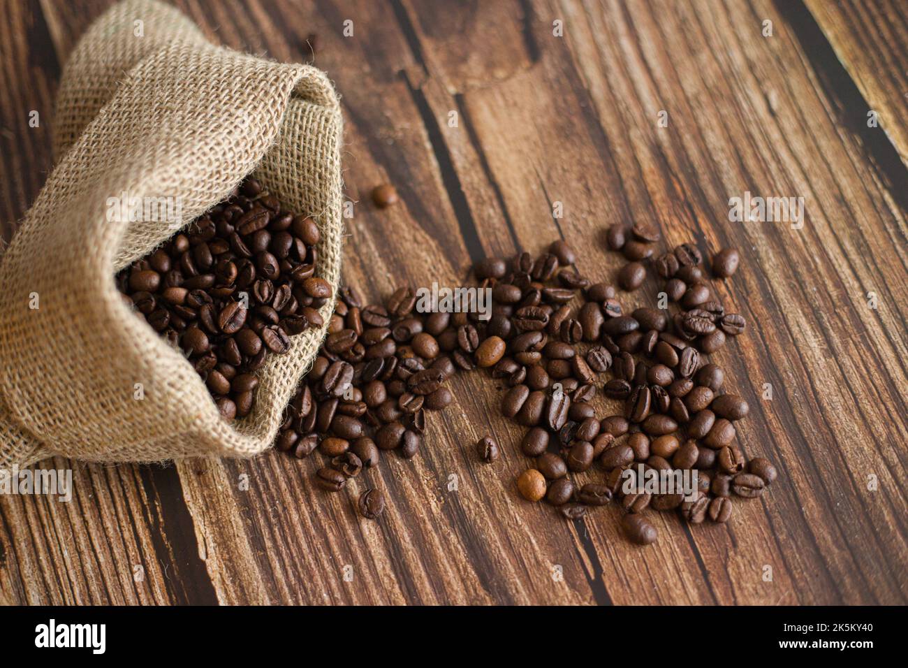 Chicchi di caffè in sacchetto di iuta e cucchiaio di legno sul tavolo Foto Stock
