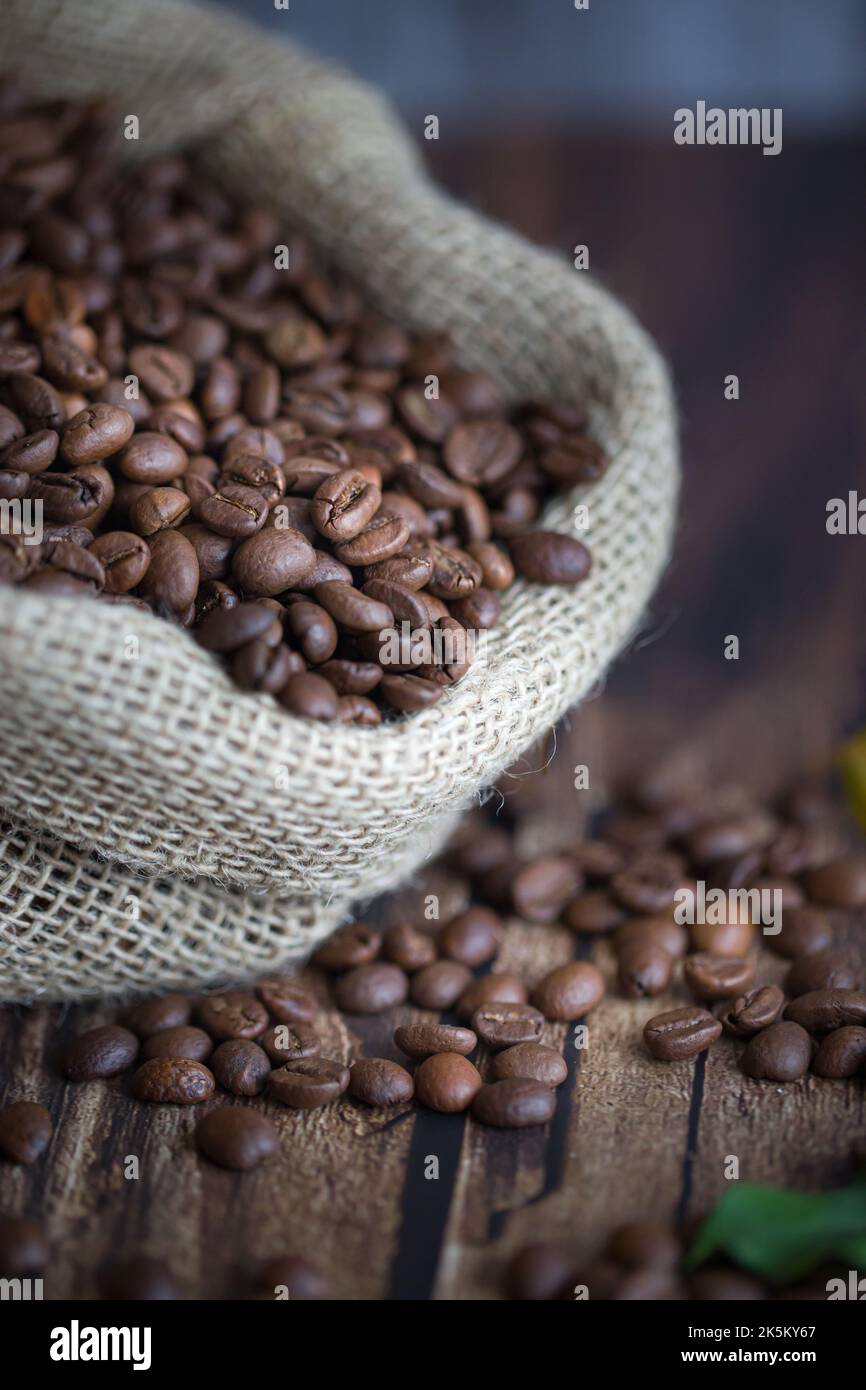 Chicchi di caffè in sacchetto di iuta e cucchiaio di legno sul tavolo Foto Stock