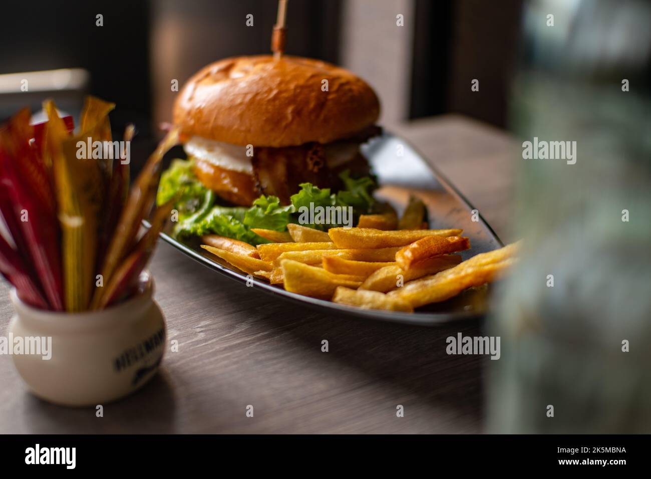 Hamburger con patatine fritte su un tavolo di legno. È una bottiglia con alcune spezie. Foto Stock