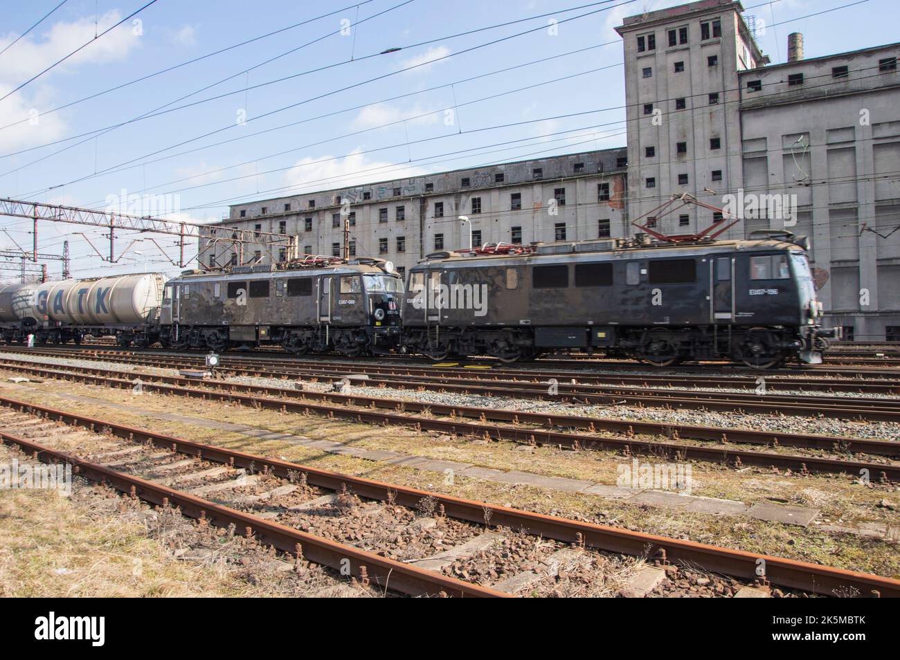 Binari ferroviari e un treno sullo sfondo di un edificio industriale abbandonato e distrutto. Foto Stock