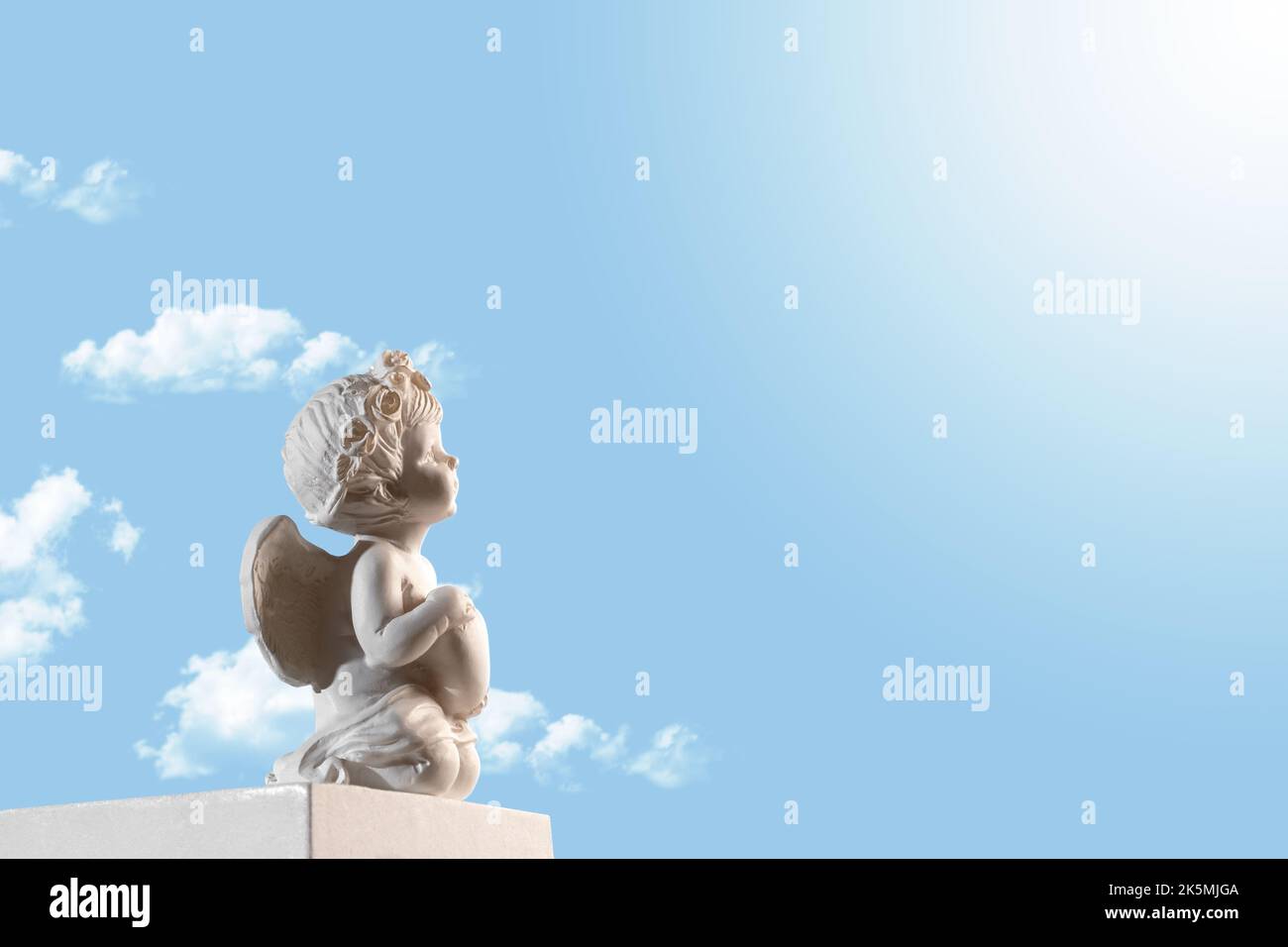 Figura di un angelo Cupido sul podio con un cuore su un cielo blu con nuvole . San Valentino. Foto Stock