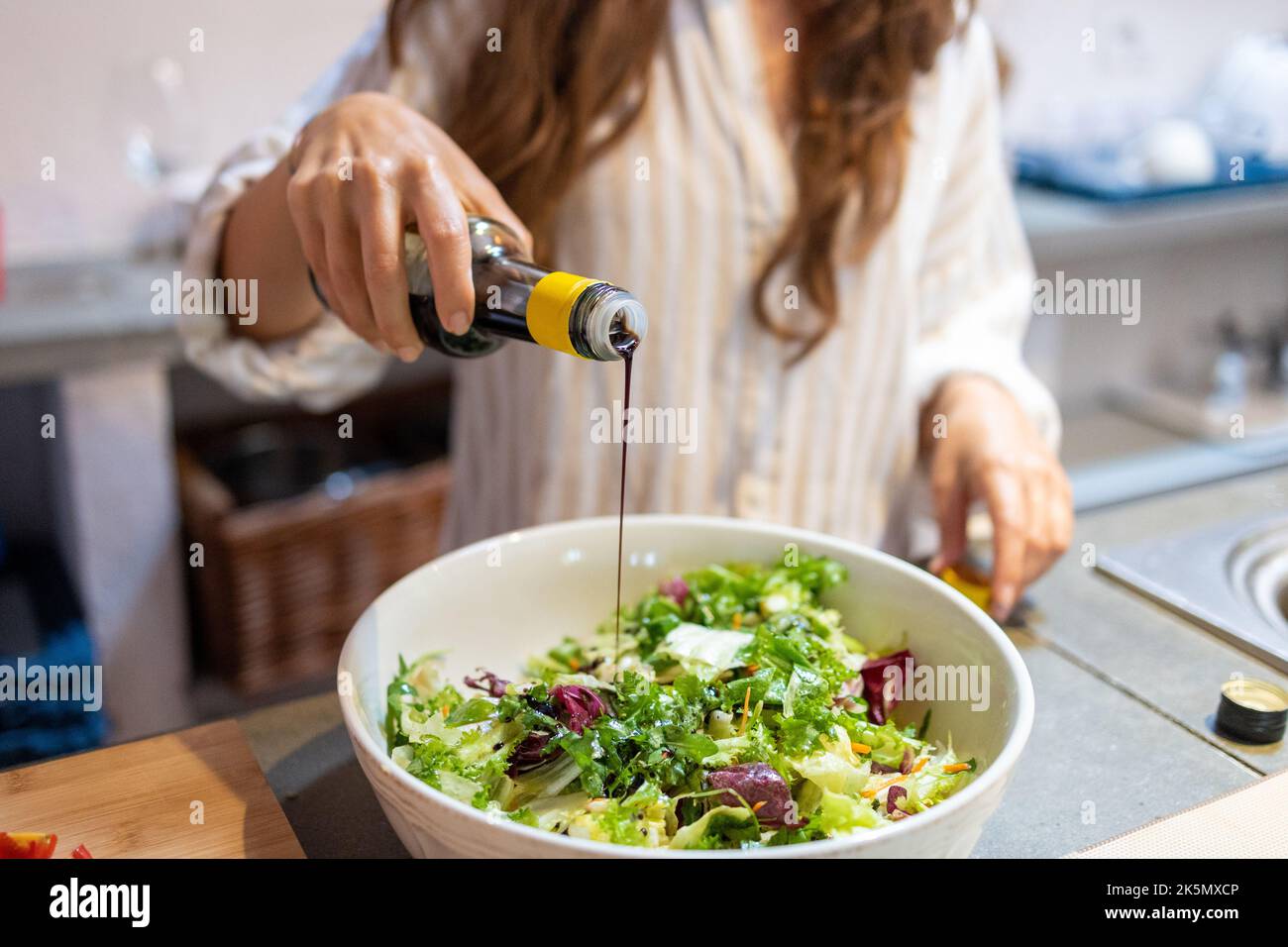 Femmina che versa l'aceto balsamico a mano sull'insalata di verdure fresche Foto Stock