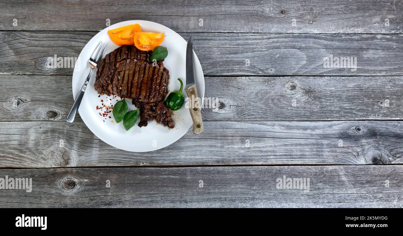 Bistecca di manzo appena grigliata con erbe e verdure su un tavolo rustico in legno a disposizione piatta Foto Stock