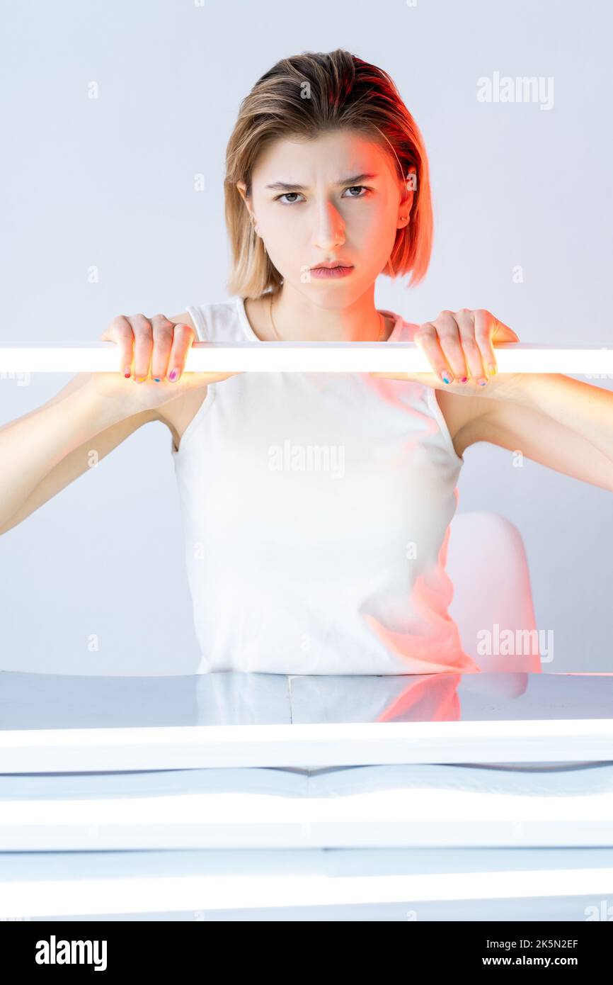 Faccia insoddisfatta. Ritratto chiaro a colori. Emozione negativa. Rosso neon bagliore infastidito infelice donna offesa con lampada a LED bianco isolato su neutro. Foto Stock