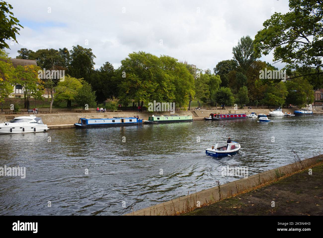 Una piccola barca di un giorno passa per barche a remi ormeggiate sul fiume Ouse a York Foto Stock