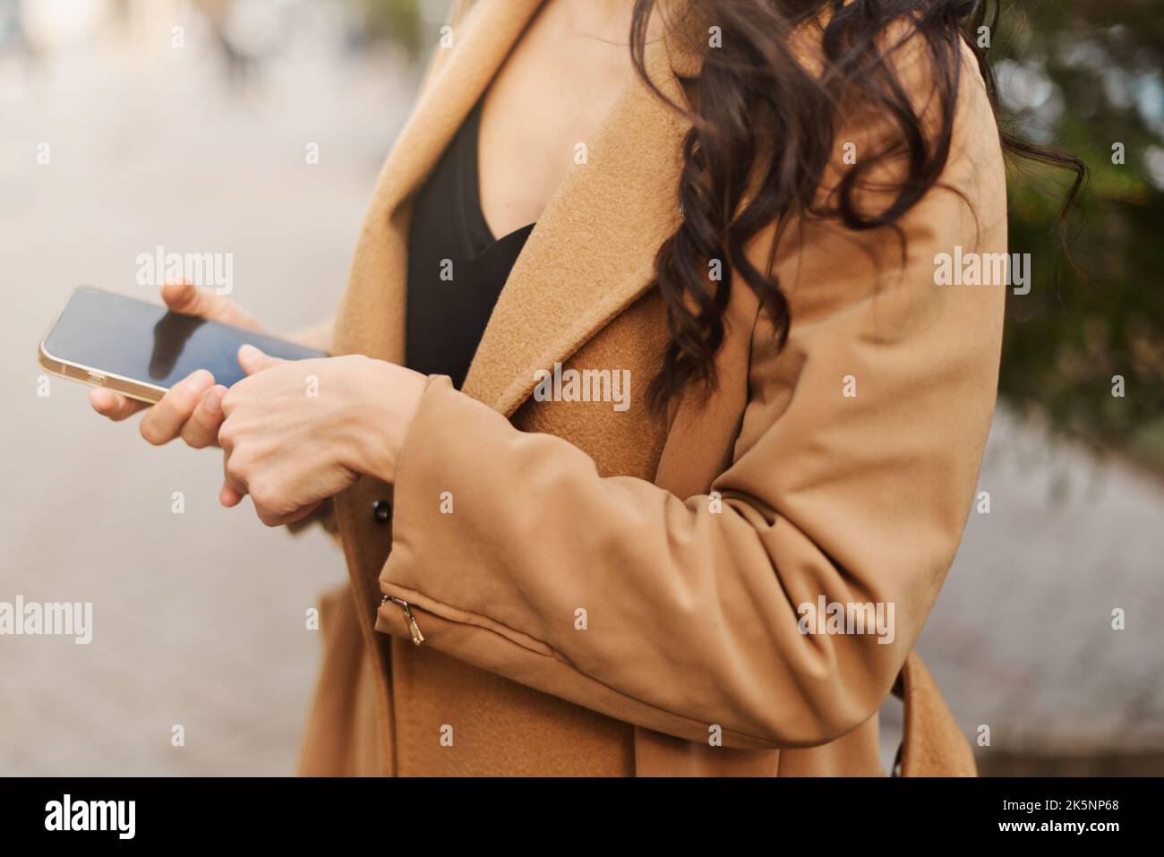Giovane bruna donna d'affari che indossa un cappotto beige con smartphone in città. Foto Stock