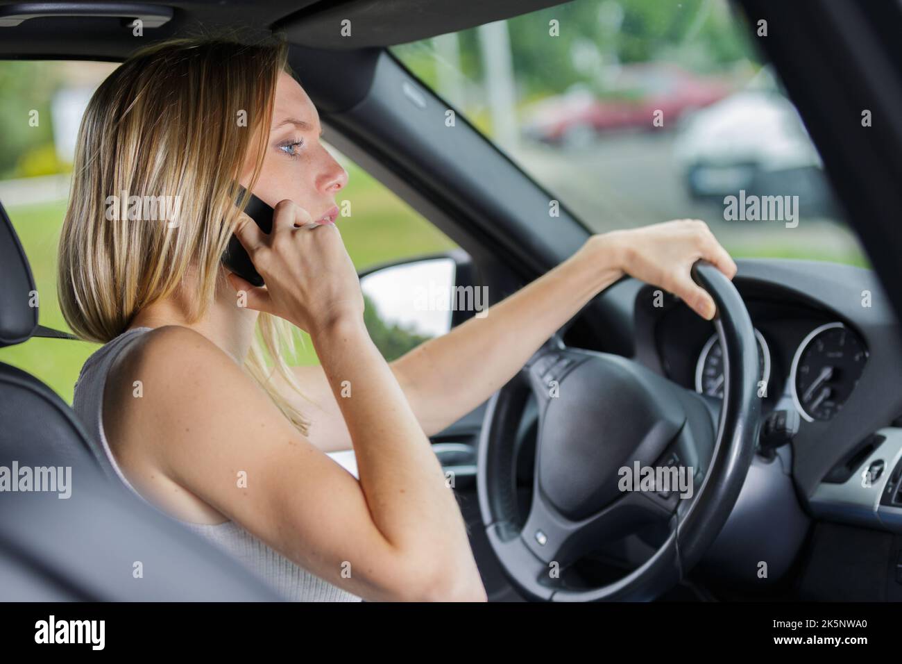 donna che parla sul telefono delle cellule mentre guida la sua automobile Foto Stock