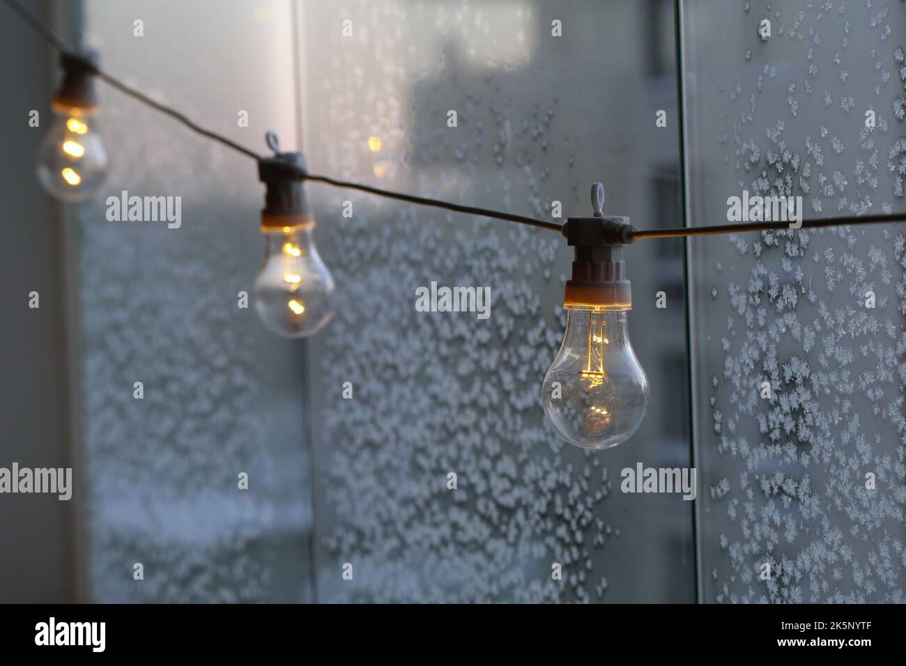 Semplice lampadina decorativa appesa su un balcone durante una giornata fredda. Vetro con cristalli di ghiaccio sullo sfondo. Energia, crisi energetica ed elettricità. Foto Stock