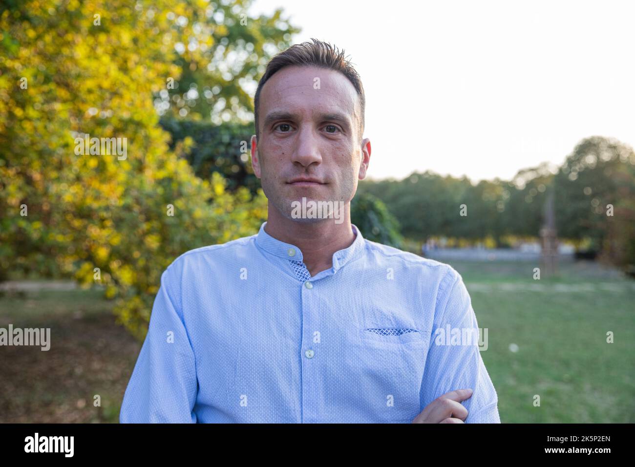 Ritratto di un uomo nel suo 30s in piedi fermo nel parco con braccia incrociate guardando la telecamera. Foto Stock