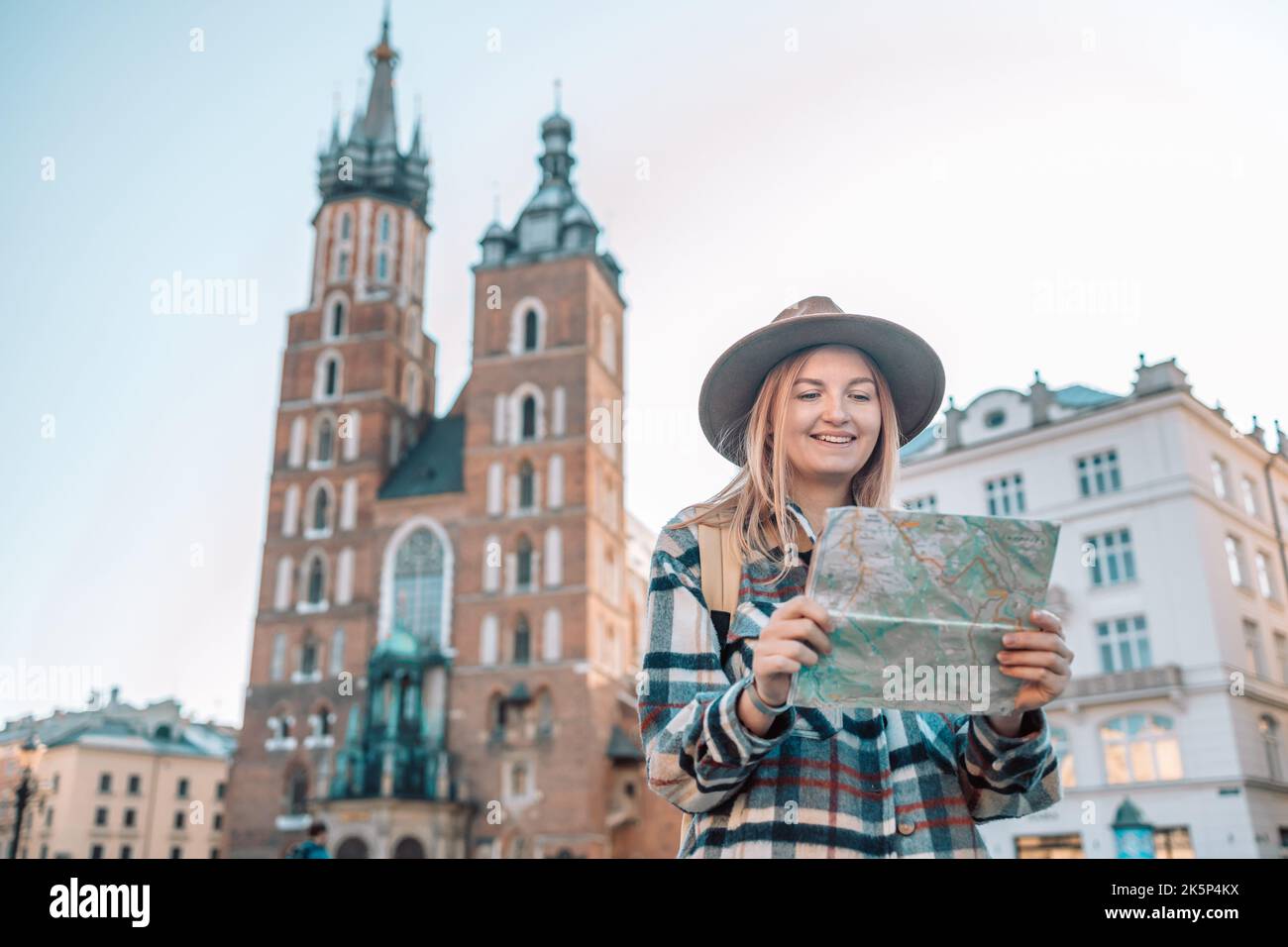 Donna allegra vagabondante con look alla moda ricerca indicazioni sulla mappa del luogo mentre si viaggia nella città vecchia di Cracovia in autunno, pianta Foto Stock