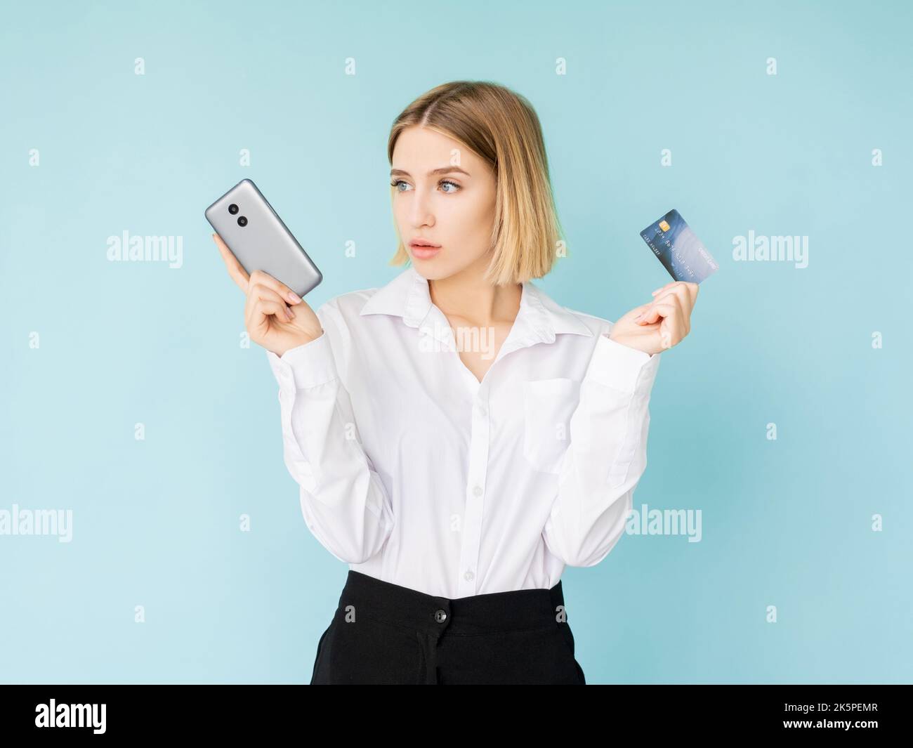 Scegli pagamenti. Funzionario bancario. Transazione online. Servizio di pass a pagamento. Puzzled donna classico look che tiene in plastica scheda e smartphone isolato blu. Foto Stock