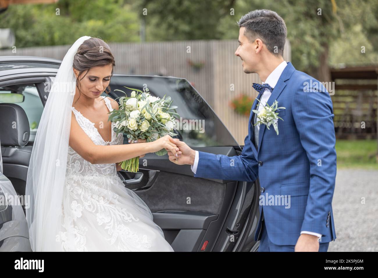 Marito di una coppia appena sposata dà una mano heloing a sua moglie che esce dalla macchina. Foto Stock