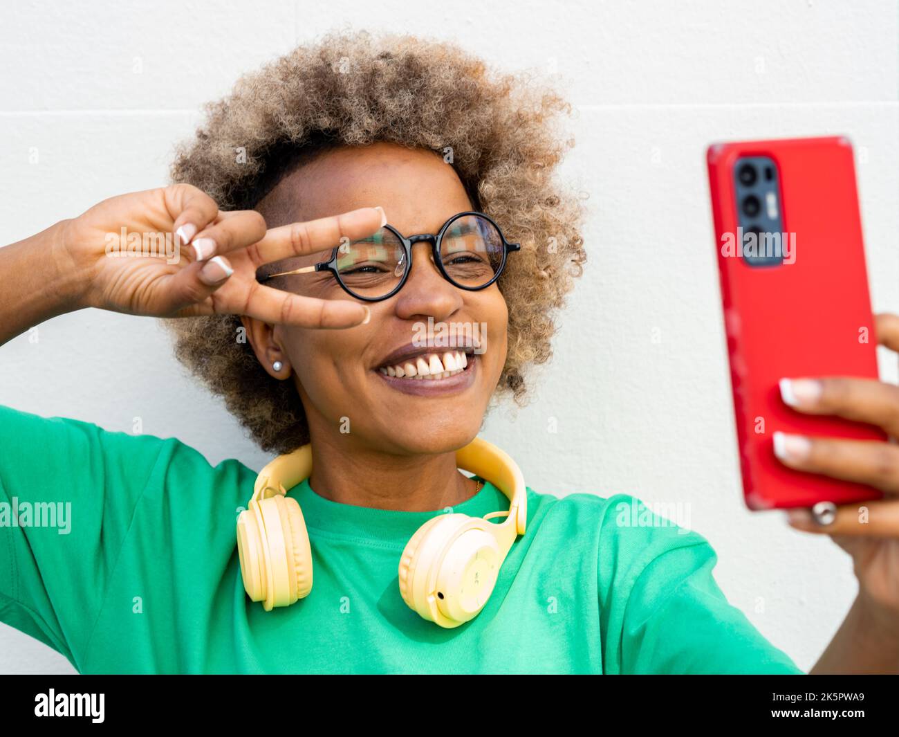 Giovane donna afroamericana sorridente con capelli afro e cuffie che prendono un selfie Foto Stock