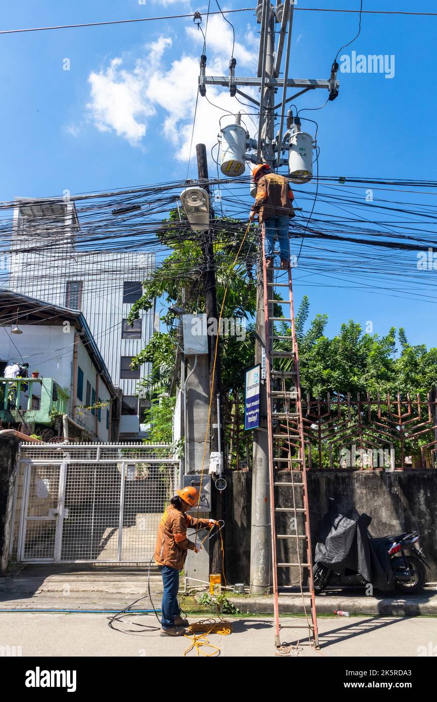 Linemen di una società elettrica che lavora su un polo elettrico a Cebu City, Filippine Foto Stock