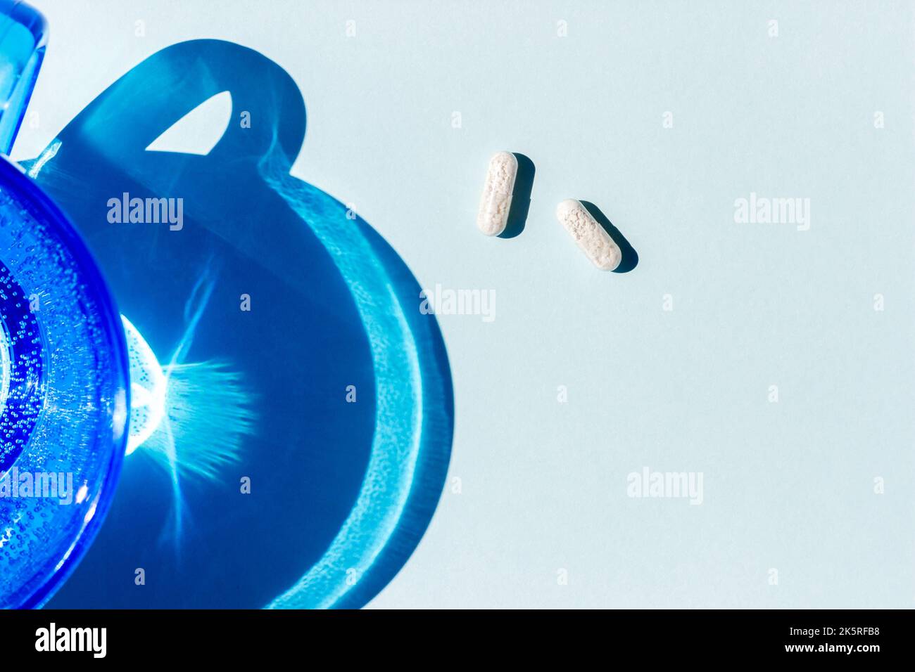 Due pillole bianche e un bicchiere d'acqua su sfondo blu con spazio copia. Medicina, concetto di assistenza sanitaria. Vista dall'alto Flat Lay. Foto Stock