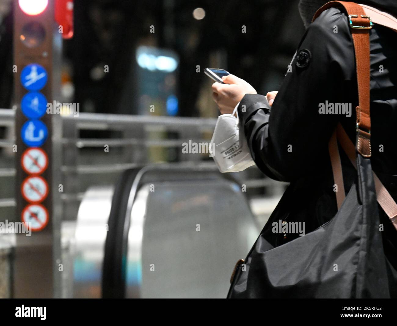 Colonia, Germania. 10th Ott 2022. Un viaggiatore indossa la protezione della bocca sul polso e digita sul suo telefono cellulare mentre aspetta il suo treno. Credit: Roberto Pfeil/dpa/Alamy Live News Foto Stock