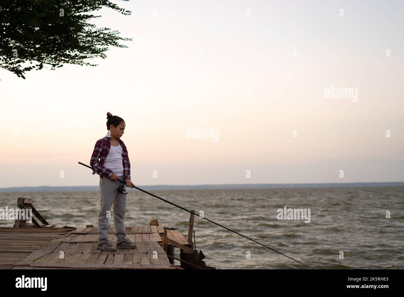 Ragazzo pesca sul lago al tramonto. Pesca bambino canna spinner in estate. Foto Stock