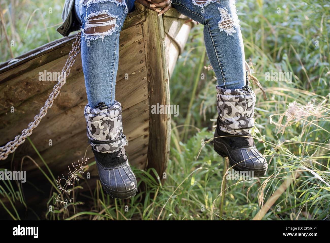 Donna africana con jeans moderni indossati siede su una vecchia barca di legno in autunno svedese Foto Stock