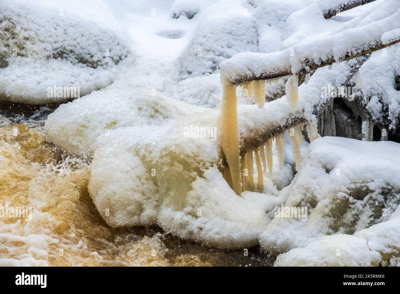 Icicle appeso su un ramo di albero in un torrente Foto Stock