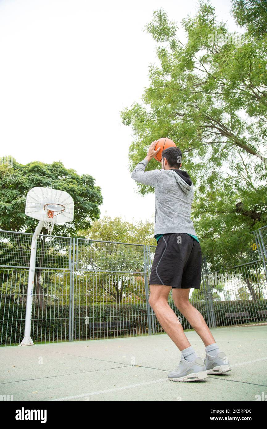 Foto verticale con vista dall'angolo basso di un uomo che lancia una palla su un campo da basket all'aperto Foto Stock