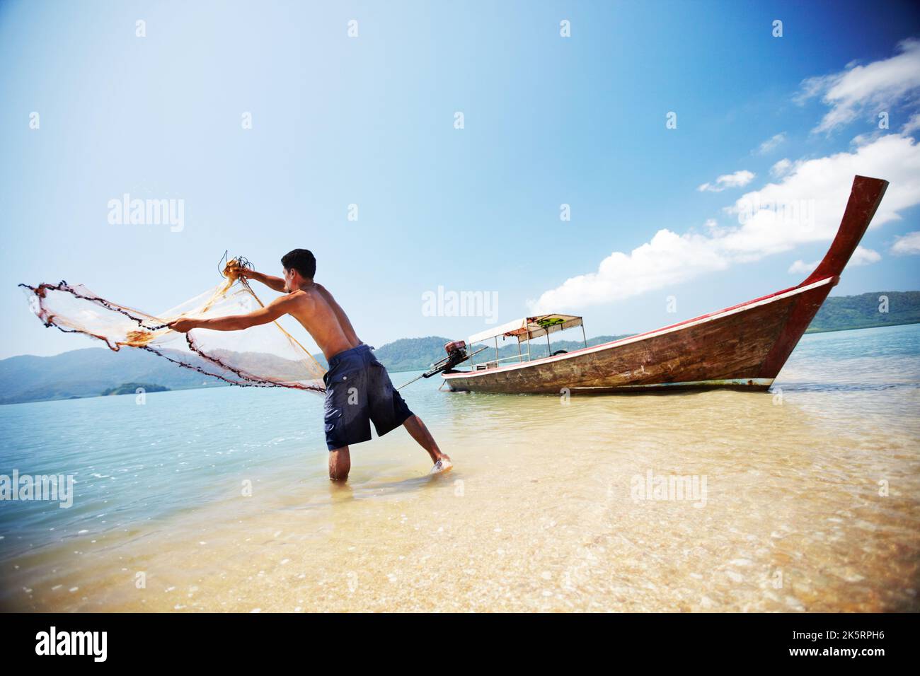 Tutto in un giorno di lavoro. Un tradizionale pescatore tailandese in piedi in acqua che getta una rete nell'oceano. Foto Stock