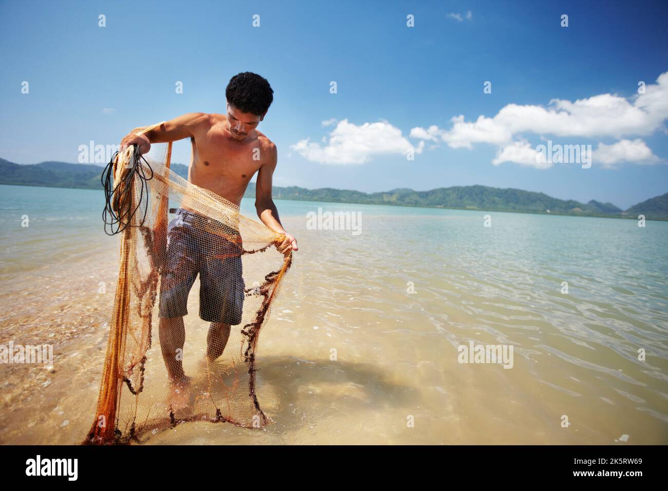 Esperto a che cosa fa. Un pescatore thailandese tradizionale in piedi nell'acqua che tiene una rete. Foto Stock