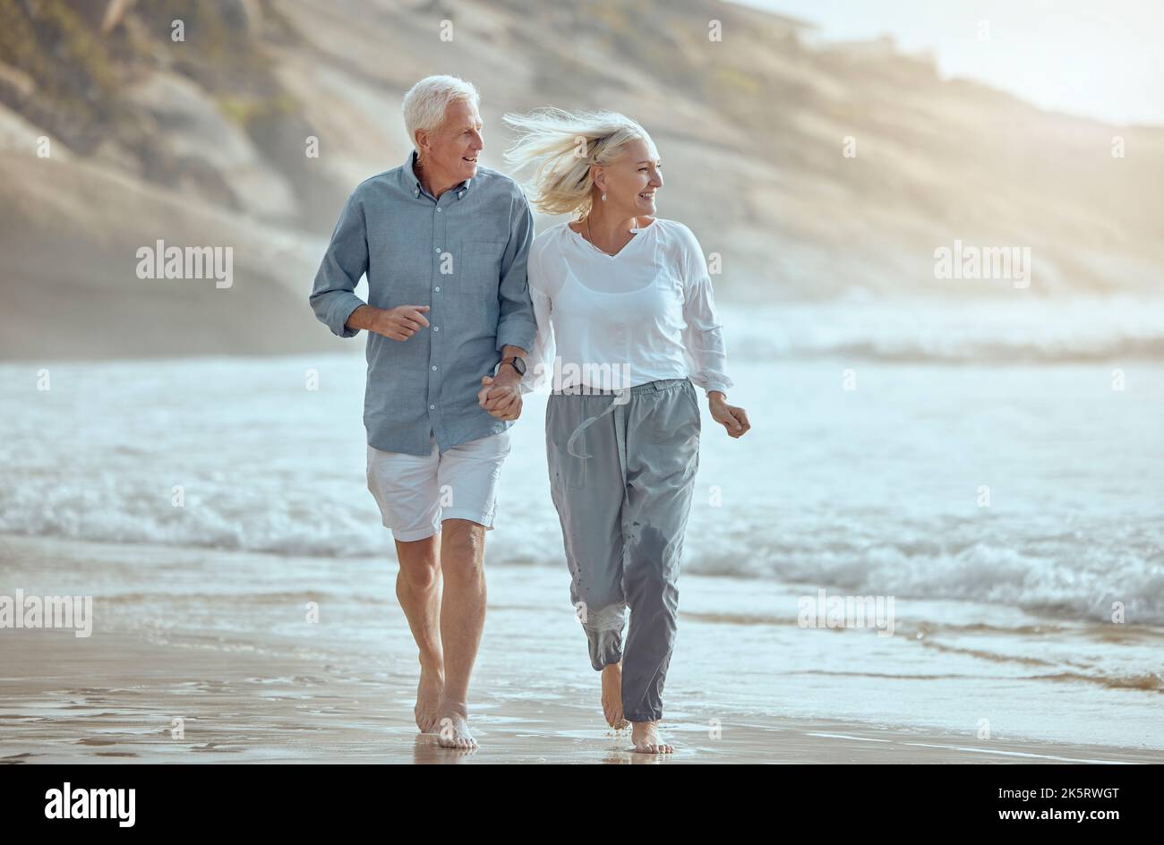 Una coppia caucasica matura felice godendo aria fresca in vacanza in spiaggia. Sorridendo coppia in pensione che ottiene un cardio workout mentre cammina fuori Foto Stock