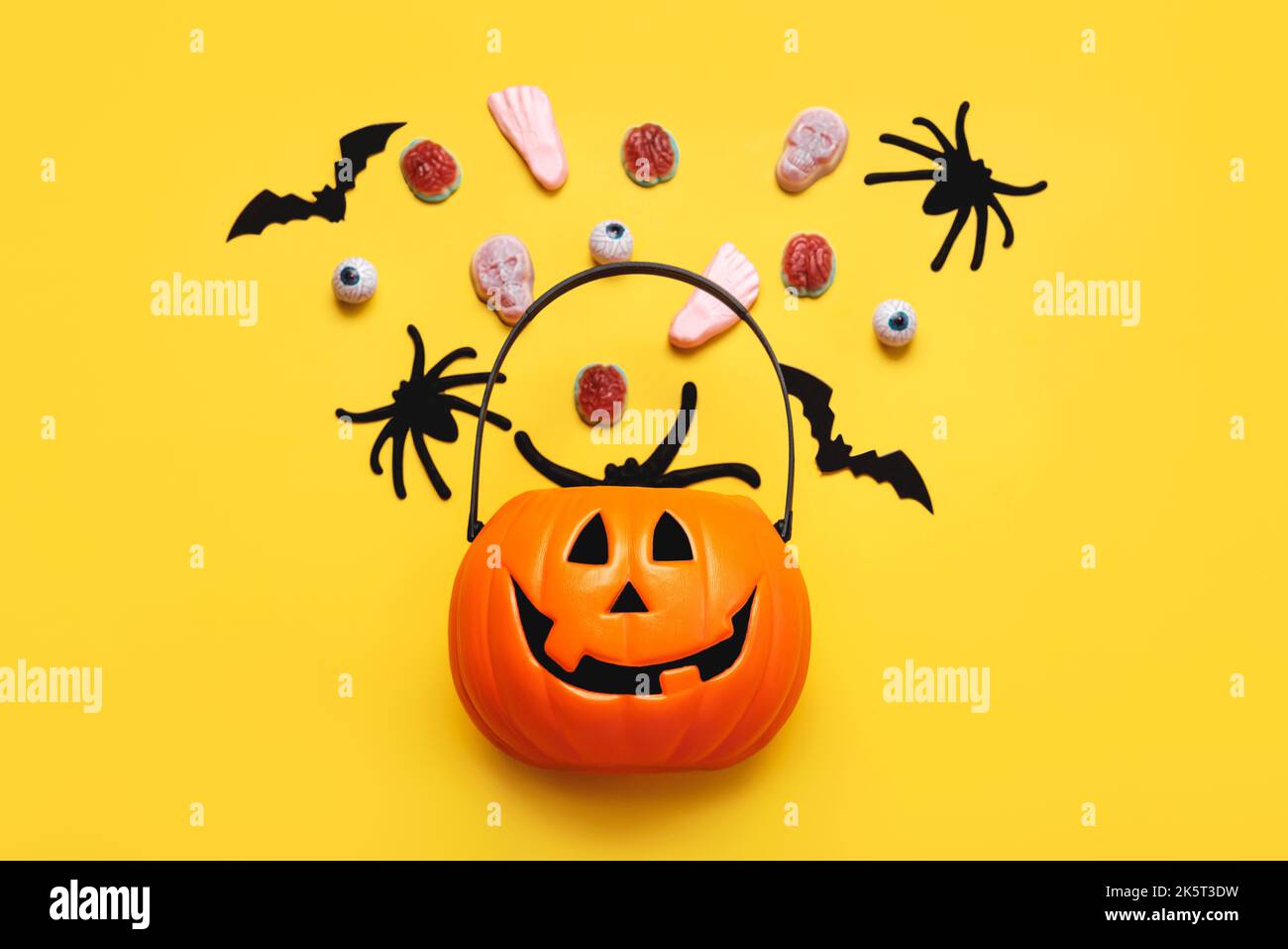 Halloween felice. Vista dall'alto del cesto di zucca di Halloween pieno di caramelle, pipistrelli e ragni su sfondo giallo. Sfondo concetto di Halloween Foto Stock