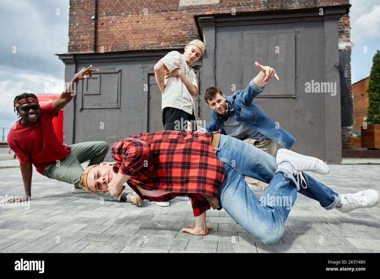 Il movimento del giovane uomo che fa il supporto pone all'aperto con tutta la squadra di breakdance maschile in background Foto Stock
