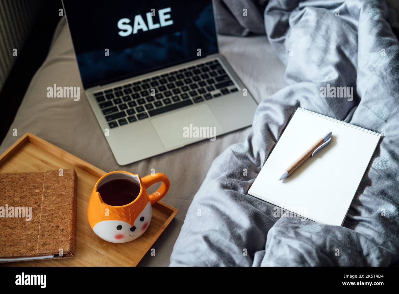 Vendita online del Black Friday. Notebook aperto vicino al computer portatile con parola sale e tè caffè tazza in cattivo casa. Preparazione allo shopping Consumer Buying Foto Stock