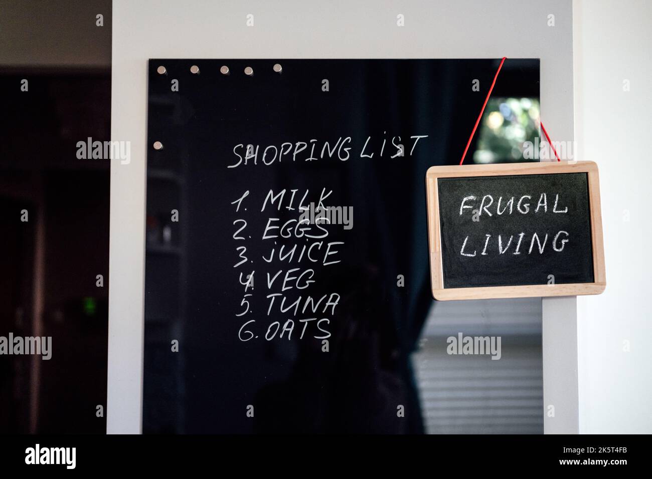 Vivere frugale, risparmiare denaro, vivere concetto a buon mercato con la lista della spesa su letterboard e Frugal testo vivente in cornice in cucina a casa Foto Stock