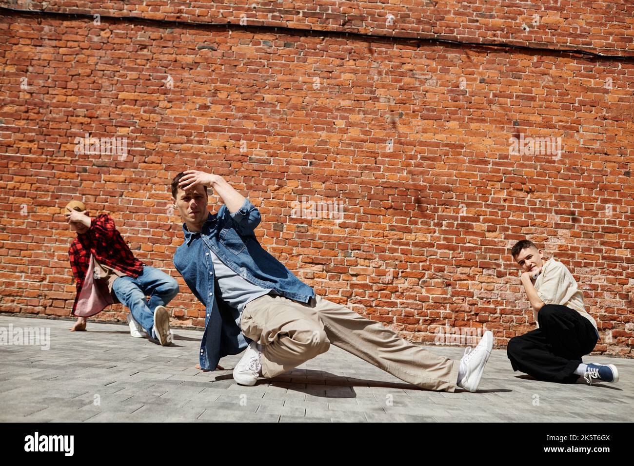 Ritratto di tutta la squadra di breakdance maschile in posa contro la parete di mattoni all'aperto alla luce del sole Foto Stock