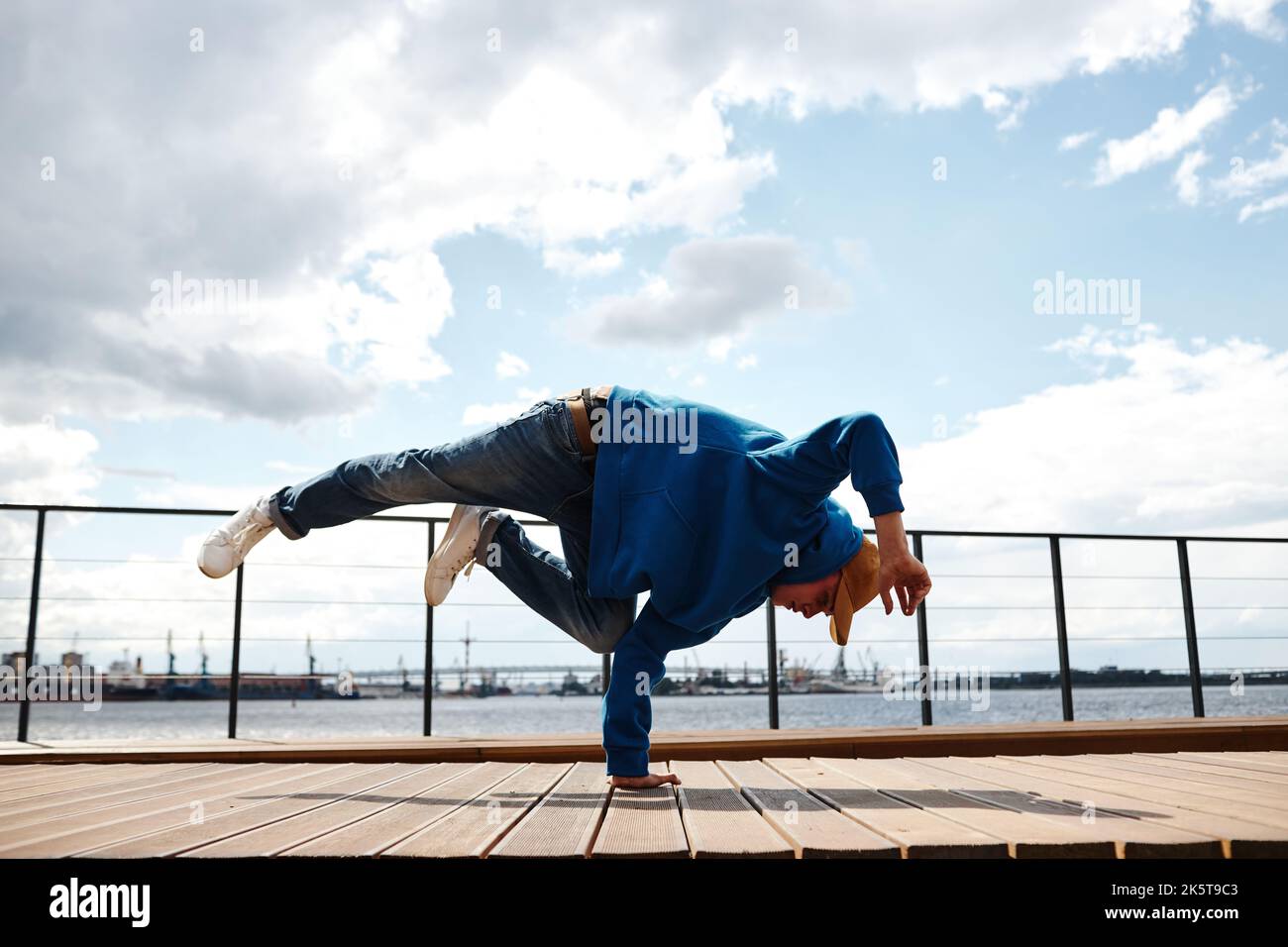 Ripresa del movimento del giovane uomo che fa la mano di breakdance posa contro il cielo all'aperto, copia spazio Foto Stock