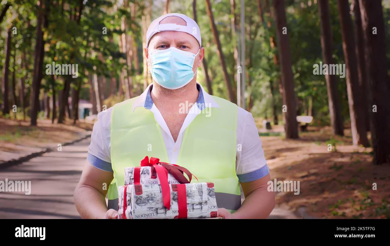 regali avvolti. uomo, corriere, in maschera protettiva, tenendo in mano diverse scatole splendidamente imballate. all'aperto. consegna di regali per eventi di festa. donazione, concetto di beneficenza. Foto di alta qualità Foto Stock