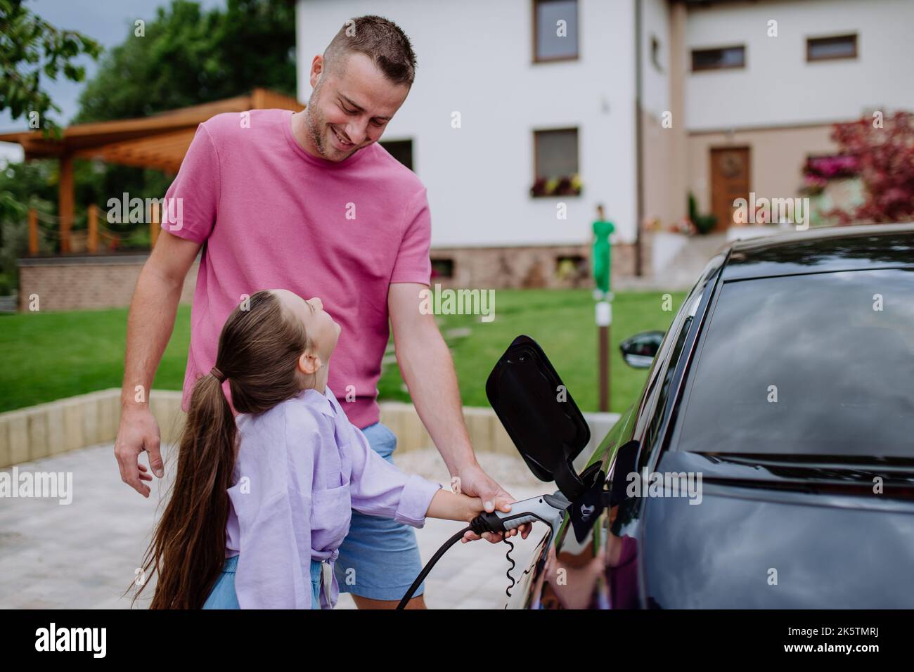 Felice padre che mostra a sua figlia come caricare la loro auto elettrica. Foto Stock