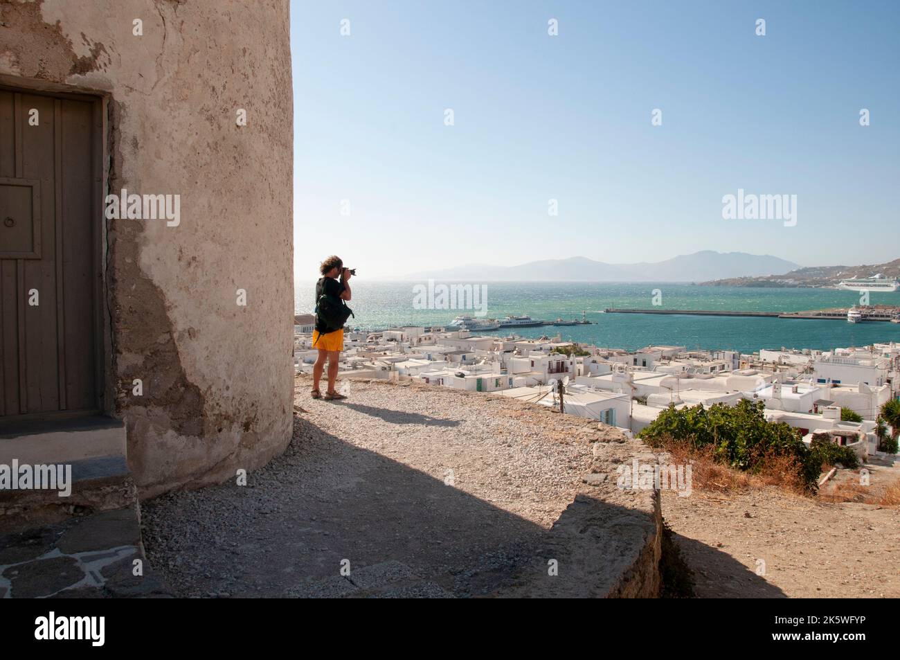 Un uomo fotografa la vista accanto a un mulino a vento tradizionale nel villaggio di Chora, isola di Mykonos, Grecia Foto Stock