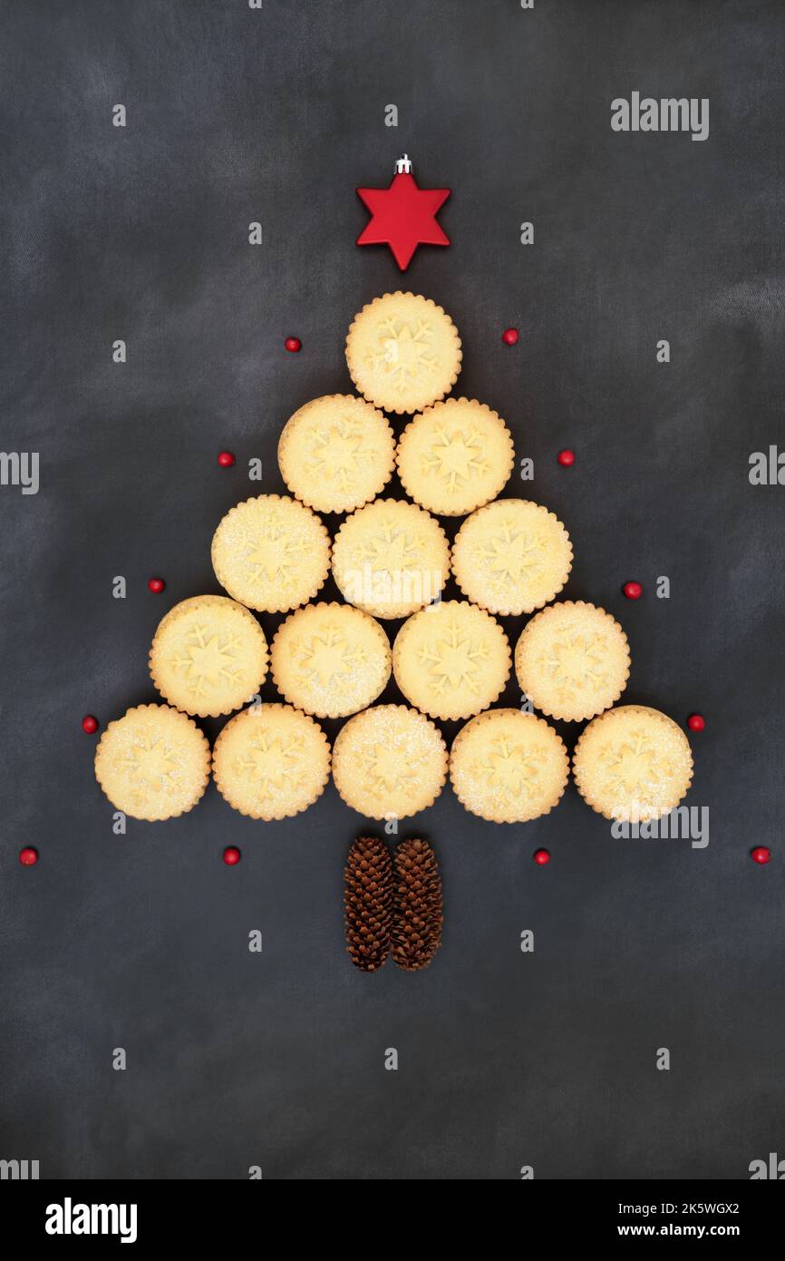 Surreale albero di Natale forma concettuale con mince torte, decorazione a stella, coni di pino e agrifoglio invernale con bacche rosse su fondo grigio grunge. Foto Stock