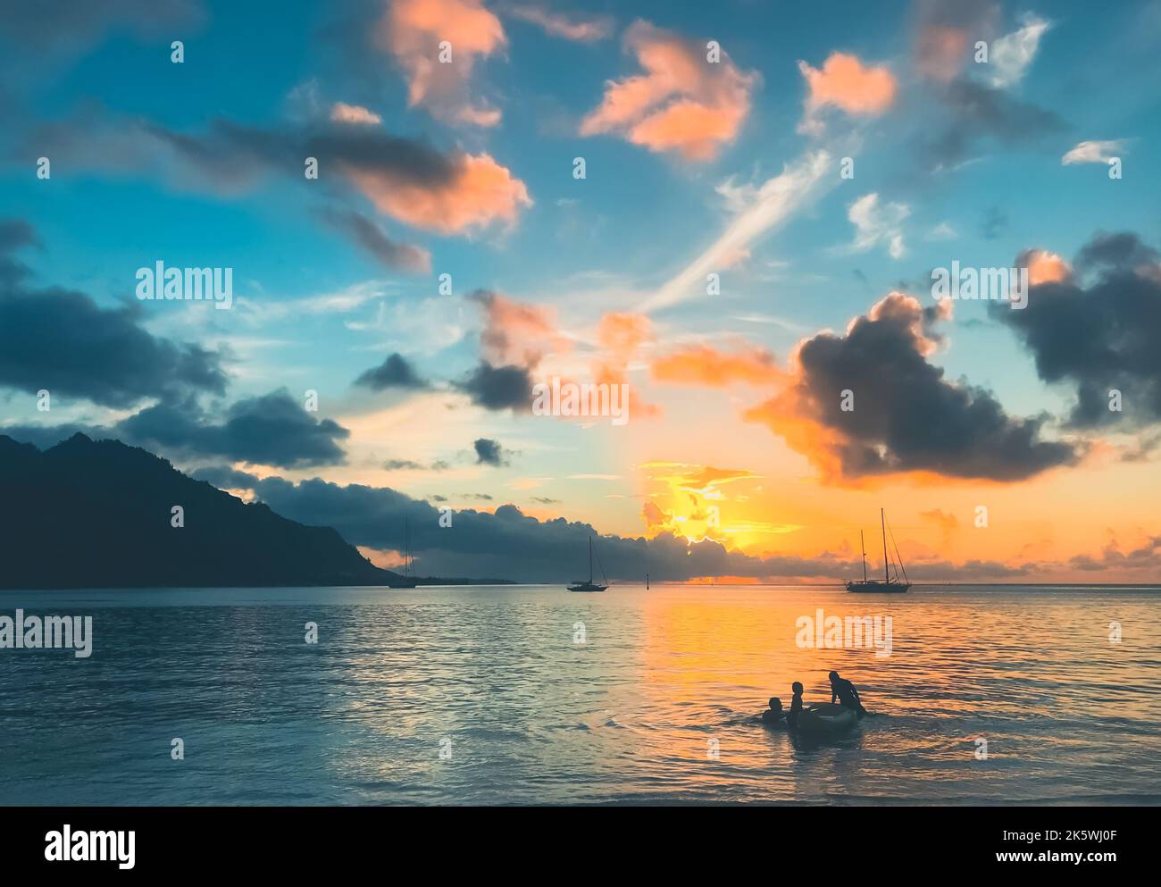 Tramonto tropico multicolore sulla calma acqua di mare. Barche a vela silhouette contro le nuvole blu arancio nel cielo, montagna sullo sfondo. Bellissimo paesaggio naturale. Viaggi, turismo, destinazione di vacanza Foto Stock